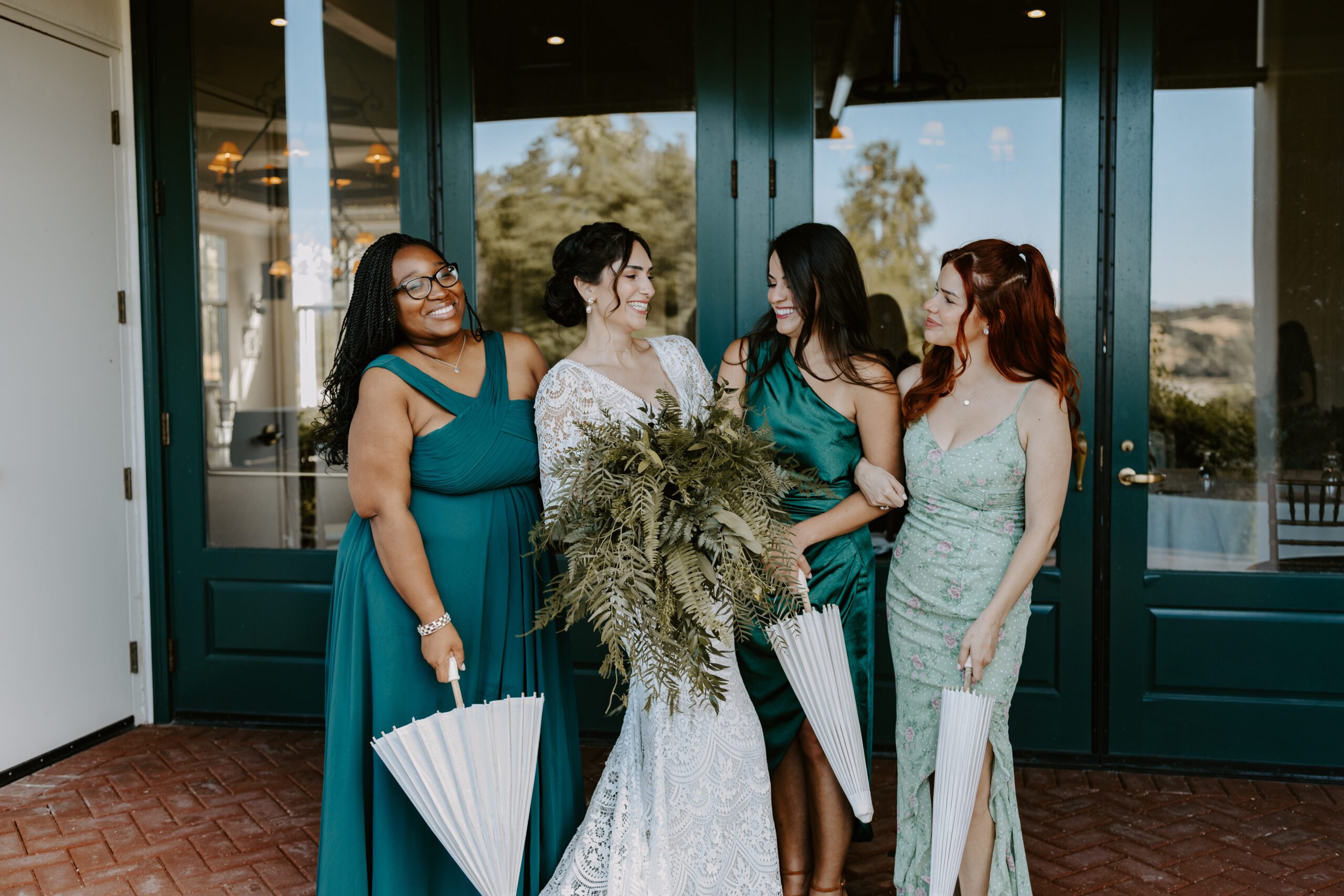 A bride surrounded by her bridesmaids laughing towards each other while holding closed parasols in their hands.