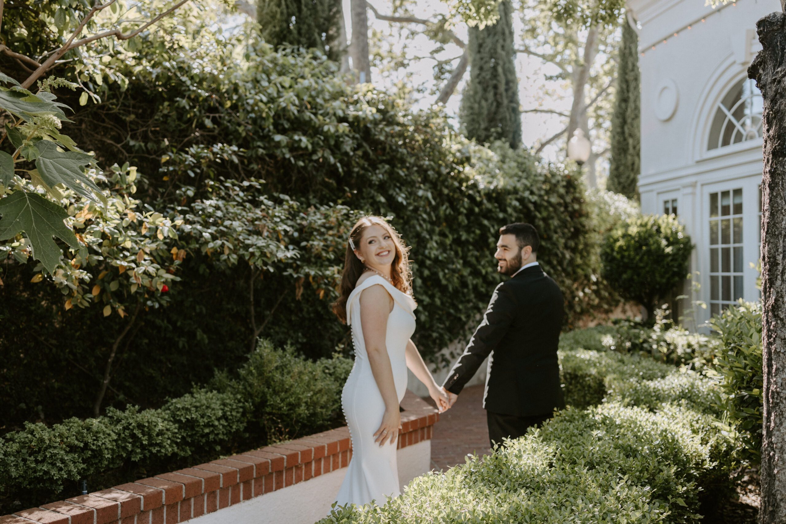Newly wed couple is walking away from couple and the Bride has turned and is smiling
