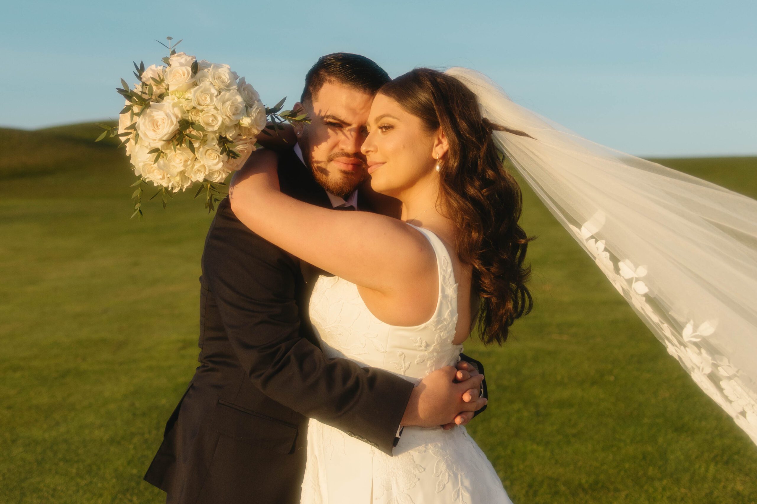 California bride and groom embracing at sunset with bouquet and flowing veil