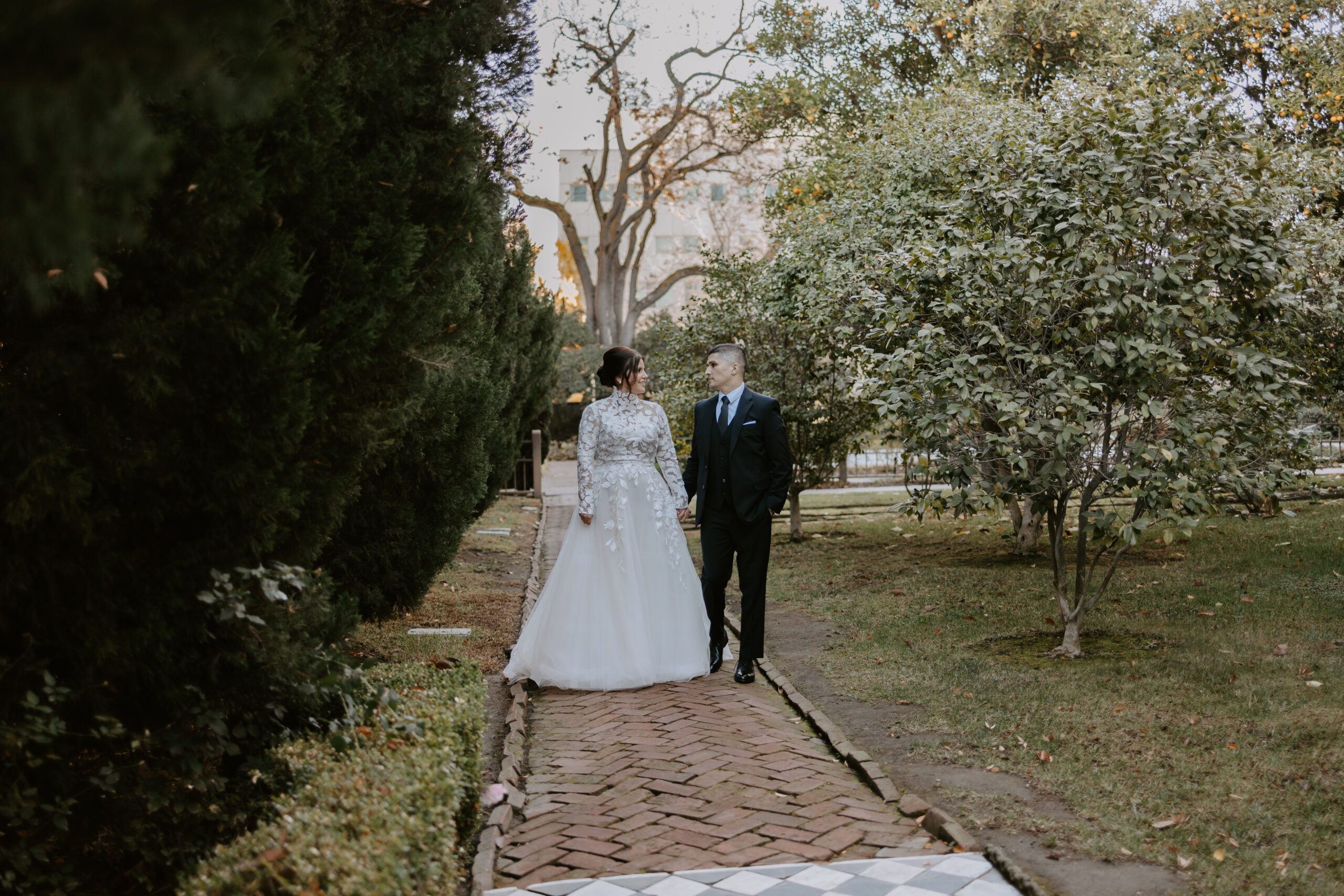 Bride and groom walking hand in hand through garden pathway